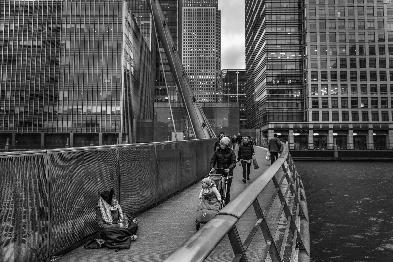 Mulher pede esmola em ponte de Canary Wharf, área que reúne bancos e empresas em Londres (no alto)