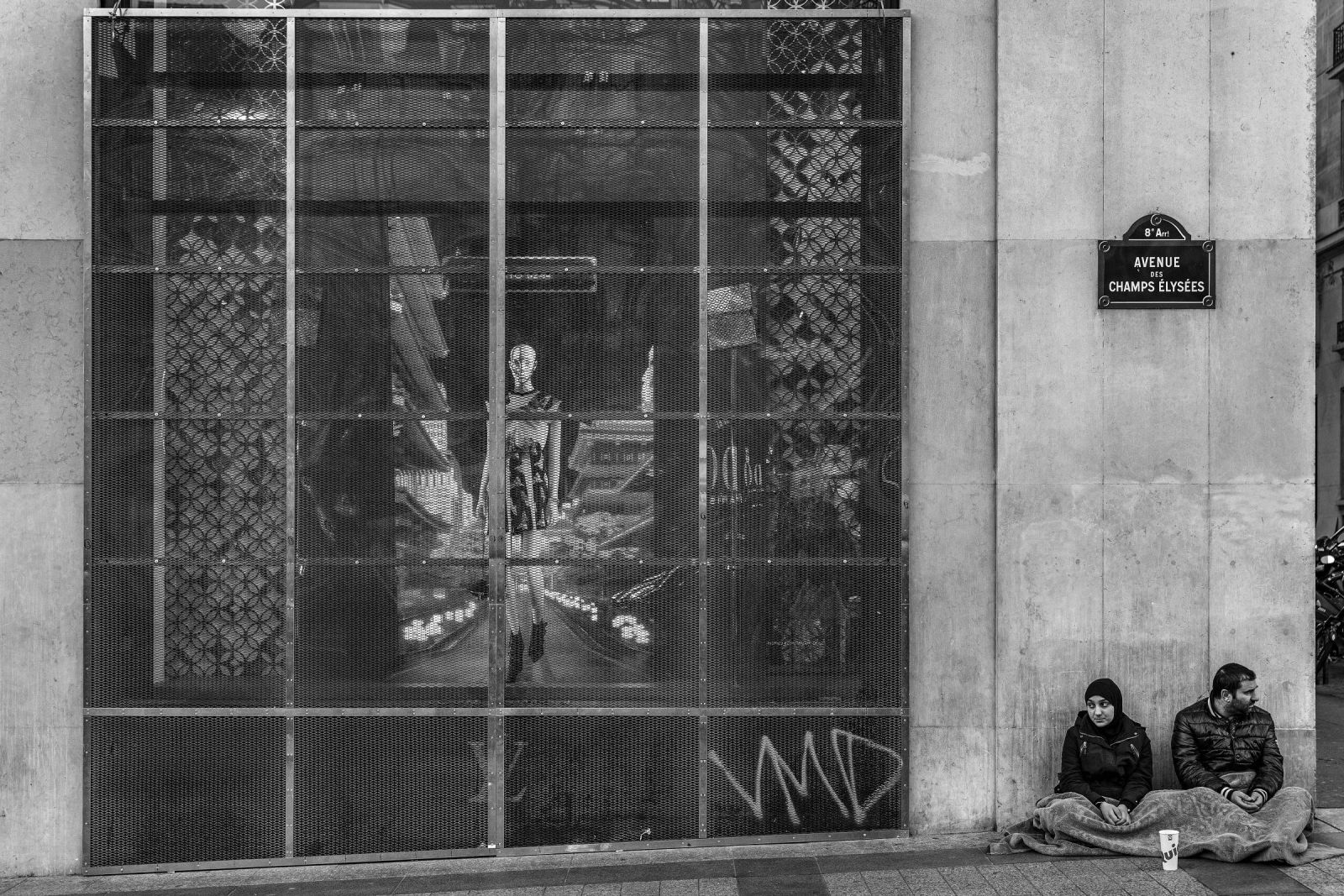 Casal pede esmola em frente a loja de artigos de luxo na avenida Champs Élysées, em Paris